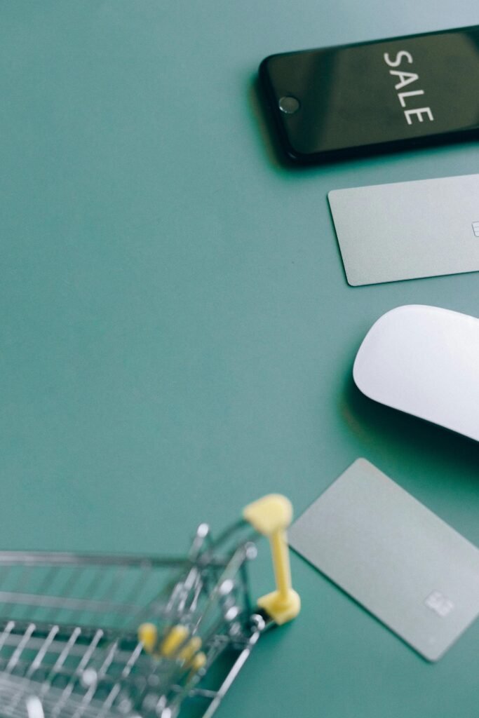 Flat lay of a shopping cart, phone with SALE display, and payment cards on a green background.